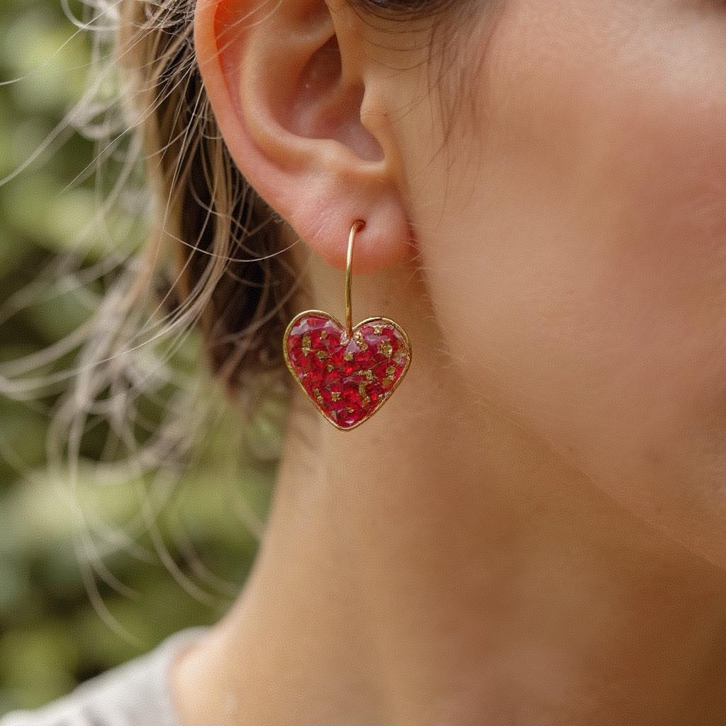 Heart-shaped earrings with red rose worn by a person outdoors.