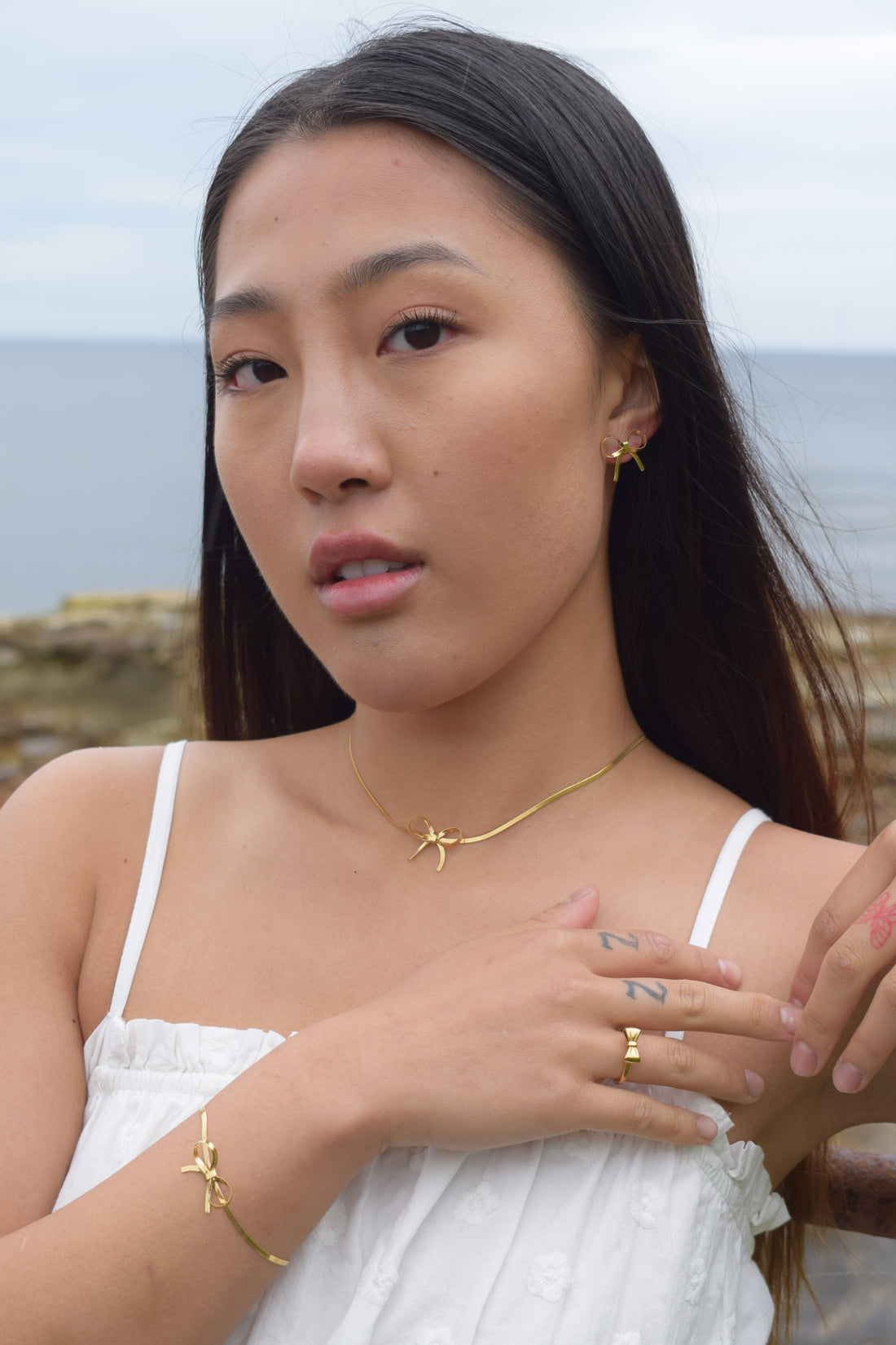 A pair of gold Mini Dancing Ribbon Earrings with a bow design, displayed on a white background.