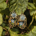 Abstract face-shaped earrings filled with colorful dried flowers, shown in gold with stainless steel hooks.
