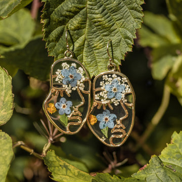Abstract face-shaped earrings filled with colorful dried flowers, shown in gold with stainless steel hooks.