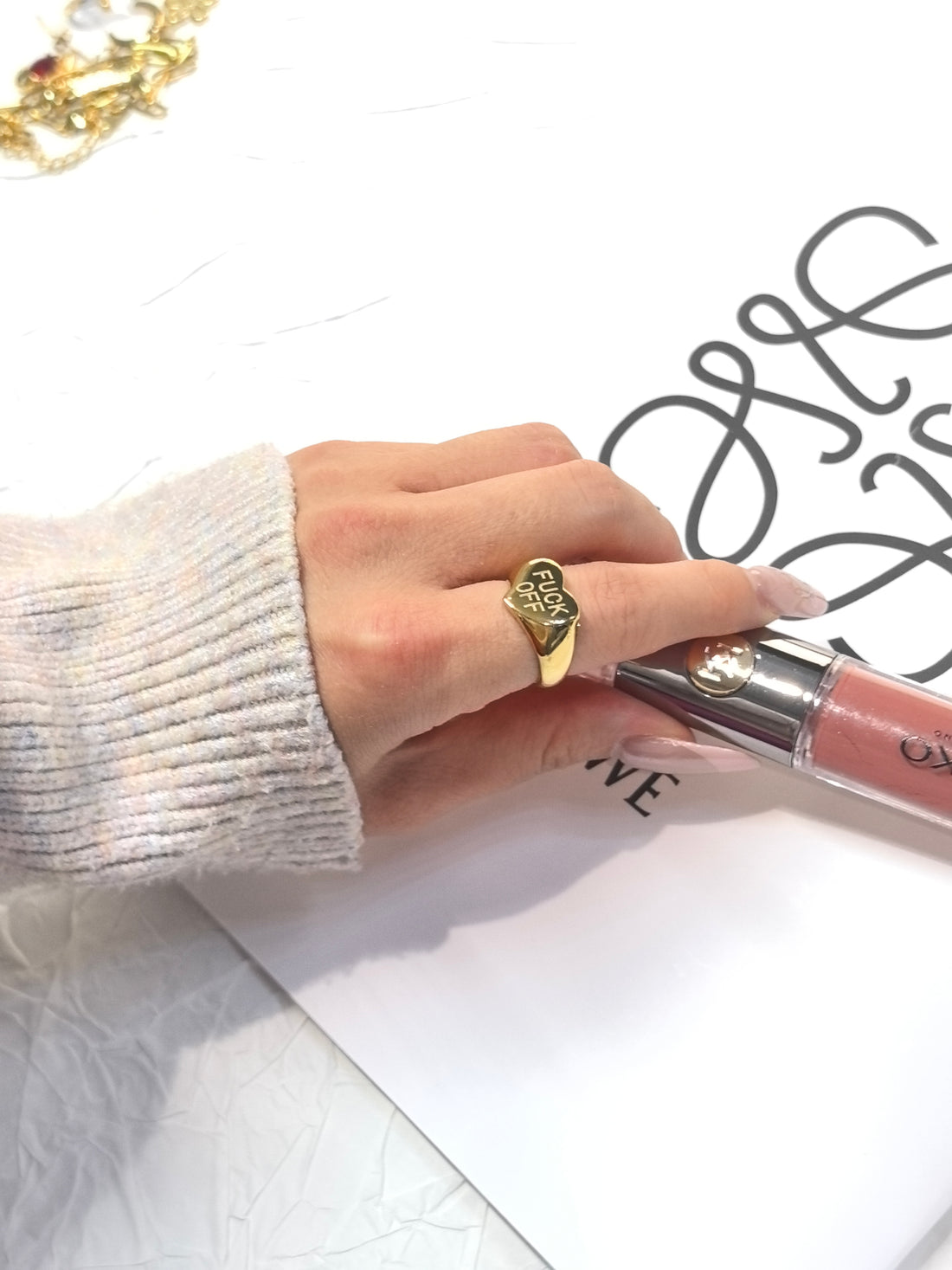 A bold gold asymmetrical heart ring engraved with “FUCK OFF".