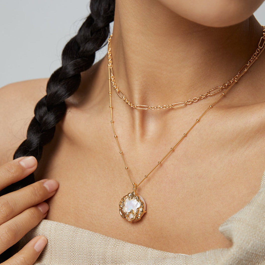 A girl wears a long necklace with a large baroque pearl and 18ct gold-plated chain.